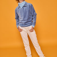 Model can be seen wearing a long sleeve ribbed knit turtleneck in a light blue color paired underneath a velour polo pullover in a dusty blue color. All paired back with basic white jeans to complete the look.