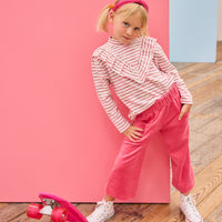 Model can be seen wearing a knit long sleeve stripe  top that features a v-ruffle detail down the center of the shirt for an elevated look. Paired back perfectly with velour pants to complete the look. 