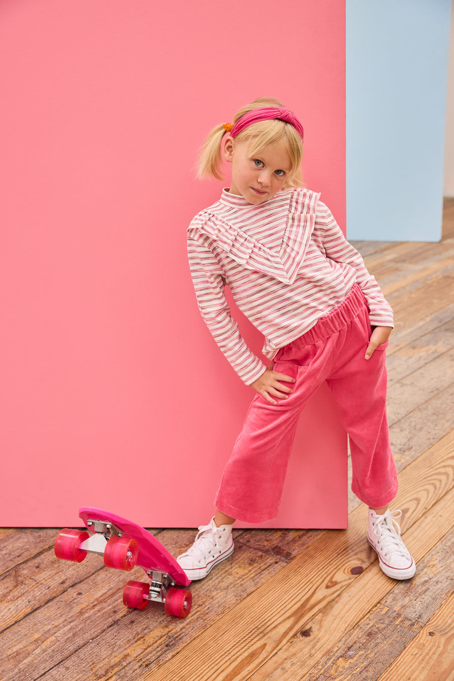 Model can be seen wearing a knit long sleeve stripe  top that features a v-ruffle detail down the center of the shirt for an elevated look. Paired back perfectly with velour pants to complete the look. 