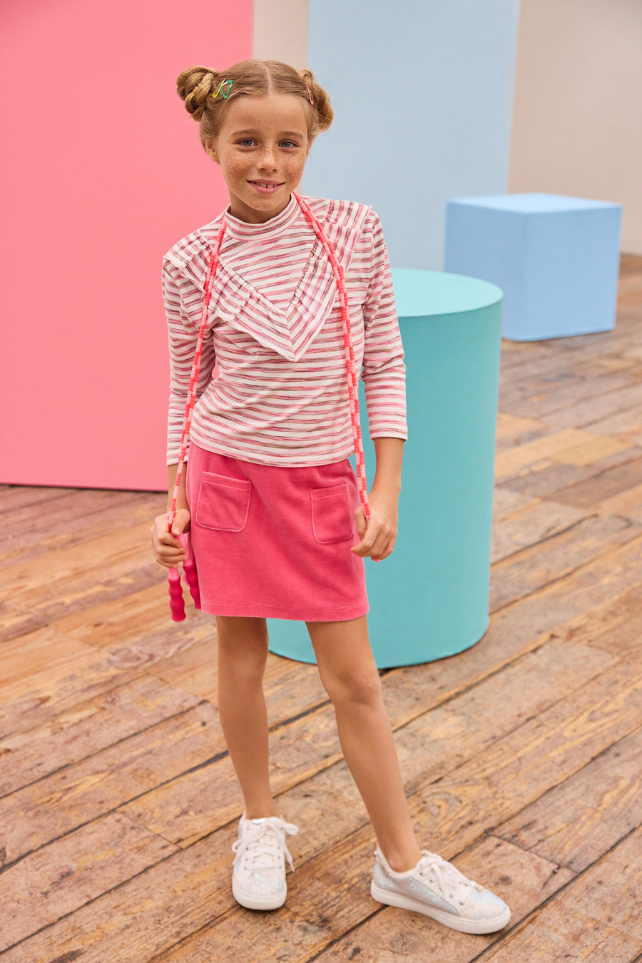 Model can be seen wearing velour skort in a beautiful pink shade that features an elastic waistband, built in shorts,  and pockets in the front for an elevated look. Pair the skort back with a long sleeve knit top with a v-detail ruffle in pink and white stripe to complete the look. 