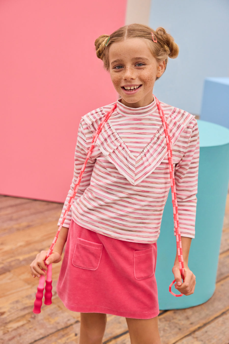 Model can be seen wearing velour skort in a beautiful pink shade that features an elastic waistband, built in shorts,  and pockets in the front for an elevated look. Pair the skort back with a long sleeve knit top with a v-detail ruffle in pink and white stripe to complete the look. 