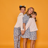 Model on left can be seen wearing white ribbed knit long sleeve top with ruffles at sleeves paired back with blue floral corduroy pants,  model in the middle can be seen wearing corduroy dress with 3/4 sleeves in the same floral print, and model on right can be seen in woven embroidered top in white paired back with same blue floral corduroy print skirt. 