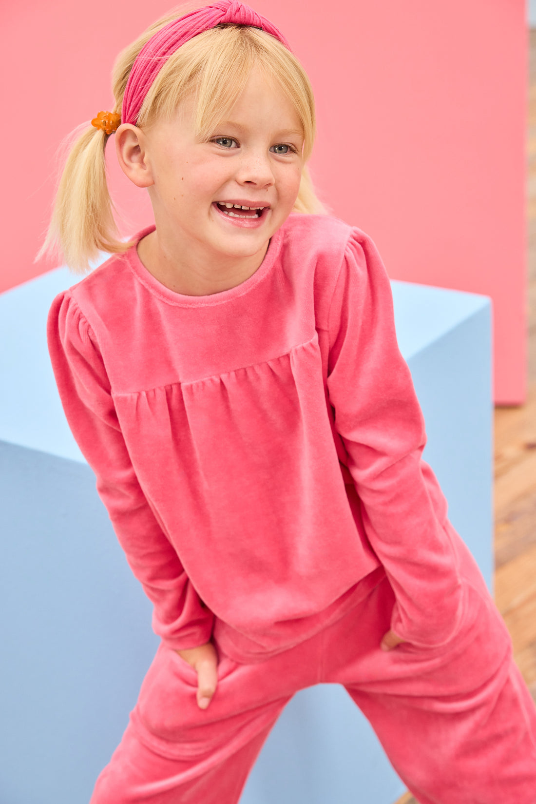 Model can be seen wearing velour long sleeve pink top that features slight pleating detail across bust for an elevated look and button closure along back of shirt. Pair back perfectly with the matching velour pants to complete the look. 