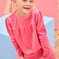 Model can be seen wearing velour long sleeve pink top that features slight pleating detail across bust for an elevated look and button closure along back of shirt. Pair back perfectly with the matching velour pants to complete the look. 