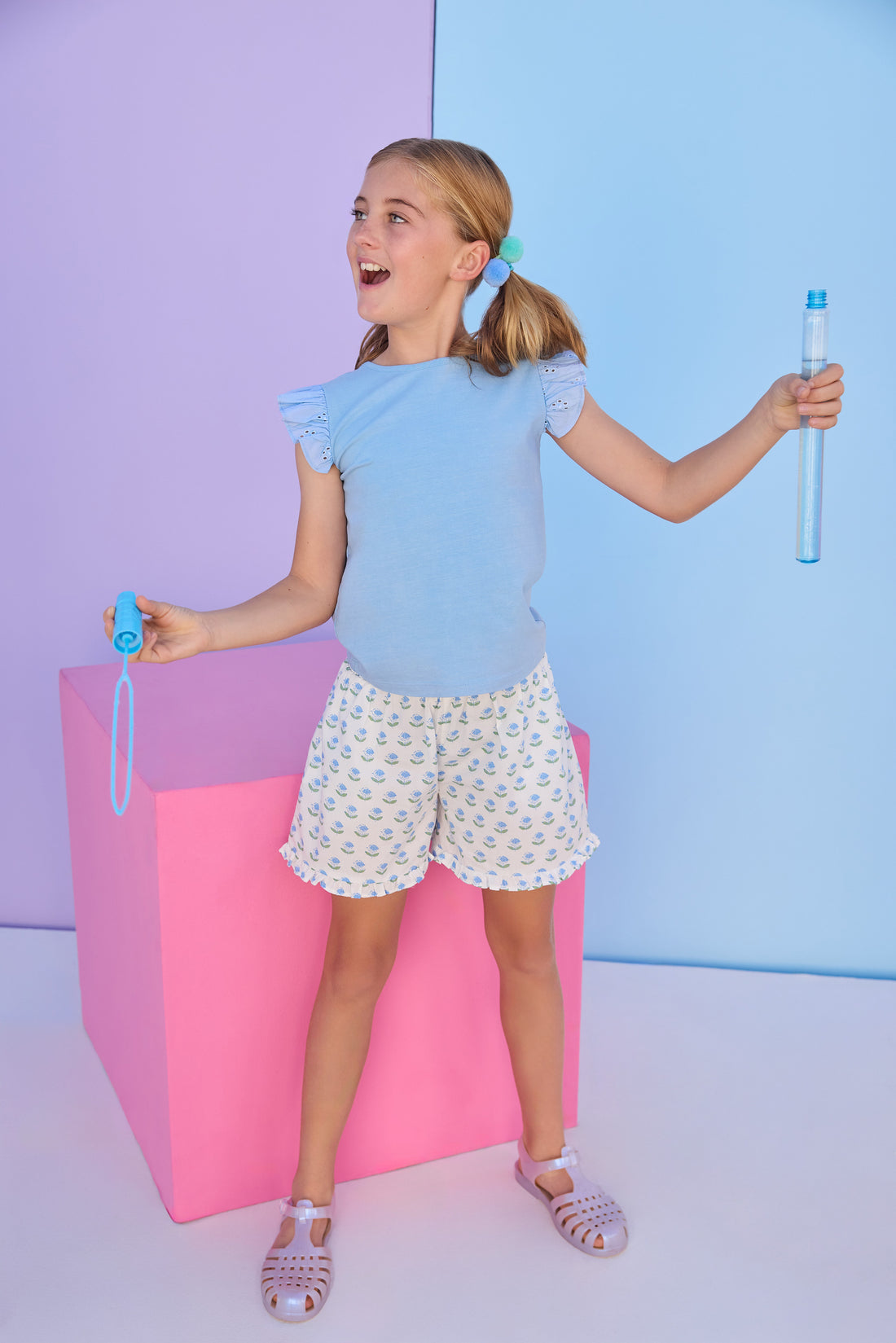 Model can be seen wearing a light blue tee that features an eyelet fabric angel sleeve detail to elevate the look. Tee pairs back perfectly with the shirred shorts in a light blue and green floral print. 