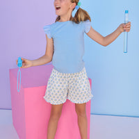 Model can be seen wearing a light blue tee that features an eyelet fabric angel sleeve detail to elevate the look. Tee pairs back perfectly with the shirred shorts in a light blue and green floral print. 