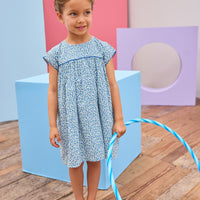 Model can be seen wearing a woven short sleeve dress in a gorgeous blue floral print that features button closures along back and blue trim detail across bust and along sleeves for an elevated look. 
