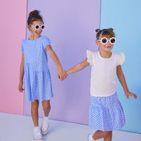 Model on right can be seen wearing a blue knit skort with a white floral design. Skort features an elastic waistband and built in shorts for a comfy but secure fit. Skort pairs back perfectly with a white knit t-shirt that features eyelet detail on the angel sleeves. Model on left can be seen wearing the same blue/white floral print knit fabric in a dress for a matching sister moment. 