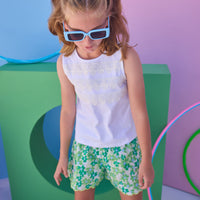 Tween model can be seen wearing shirred shorts in a green/light blue floral print. Shorts feature smocking along waist and scallop edges to elevate the look. Paired back perfectly with a white knit tank top with fun lace features across chest to complete the look. 