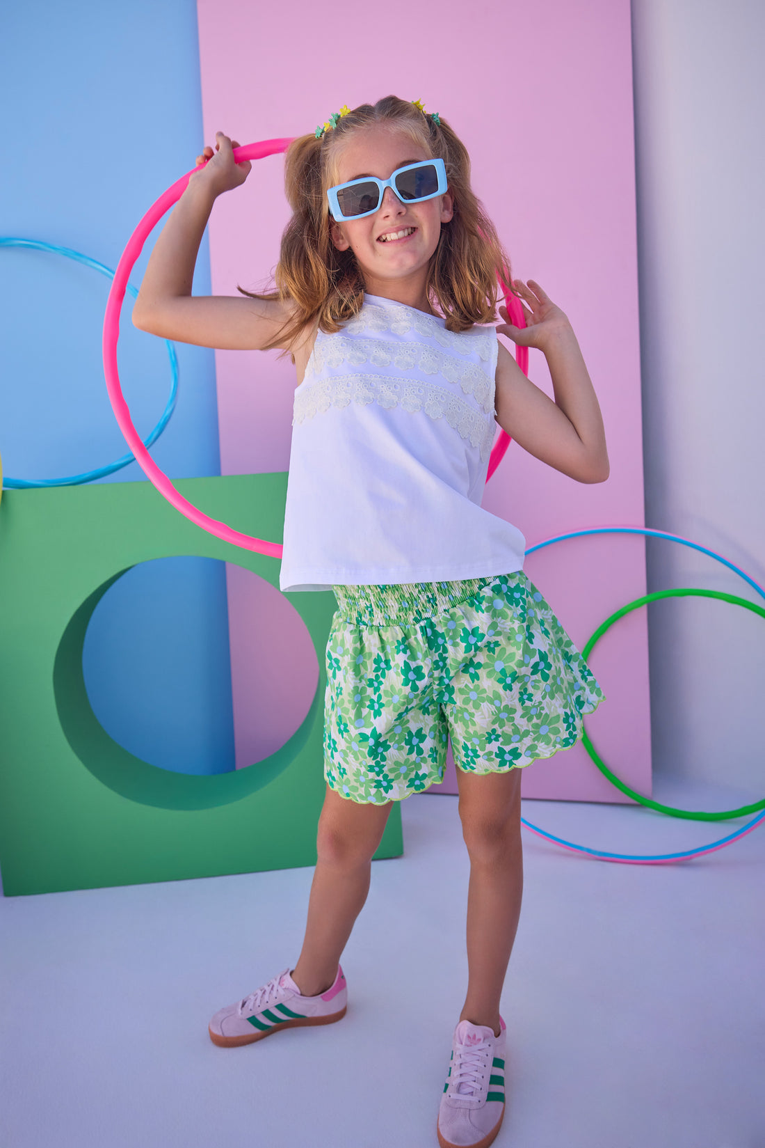 Tween model can be seen wearing a white knit tank top that features lace detailing across the bust of the shirt to give it an elevated look. Top pairs back perfectly with shirred scallop shorts in blue and green floral to complete the look. 