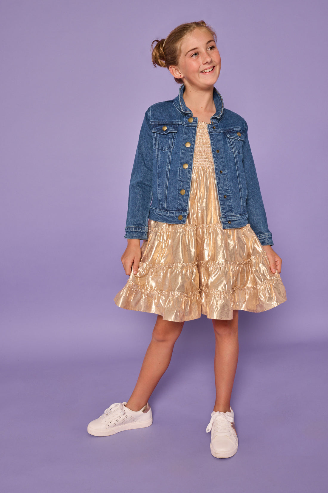 Model can be seen wearing a gold metallic dress with smocking detail at bust and tier details across body. Paired underneath our jean jacket to complete the look. 