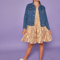 Model can be seen wearing a gold metallic dress with smocking detail at bust and tier details across body. Paired underneath our jean jacket to complete the look. 