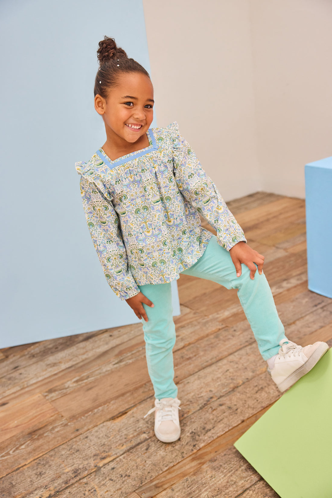Model can be seen wearing a beautfiul green/aqua/yellow floral top that features a square neck and angel sleeves to elevate the look. Top pairs back perfectly with aqua twiggy pants to complete the look. 