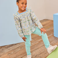 Model can be seen wearing a beautfiul green/aqua/yellow floral top that features a square neck and angel sleeves to elevate the look. Top pairs back perfectly with aqua twiggy pants to complete the look. 