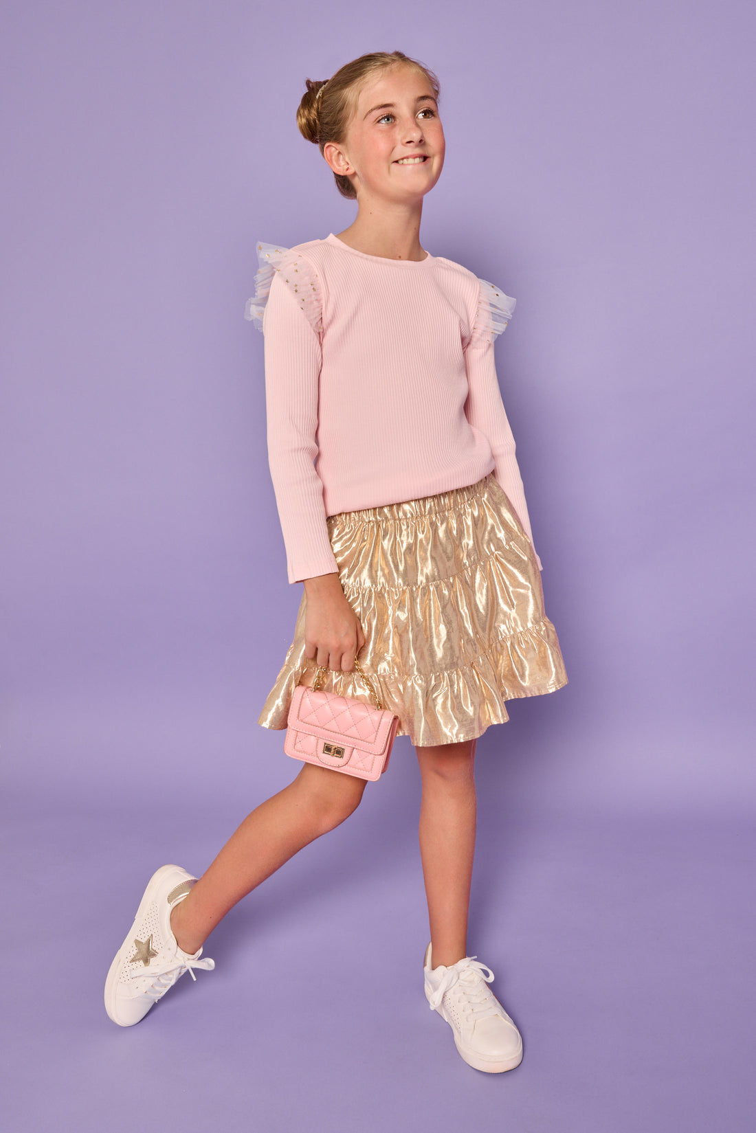Model can be seen wearing a bubblegum pink ribbed knit long sleeve t-shirt with tulle sparkle star fabric at top of sleeves for elevated look.Paired back with a gold skort in a metallic lurex material that has built in shorts for a secure fit. 