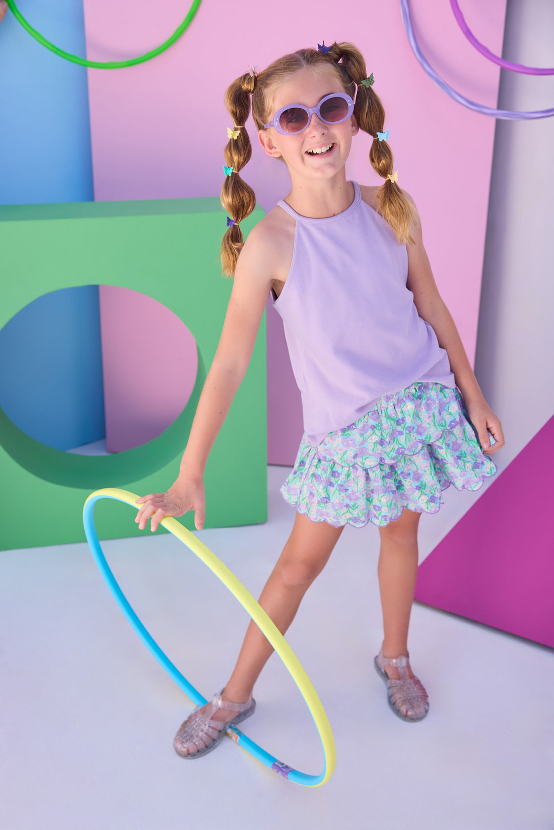 Model can be seen wearing a lavender halter tank top that features button closure along back and is made of a stretchy knit fabric. Top pairs back perfectly with tiered skort in the purple/aqua/green floral to complete the look. 