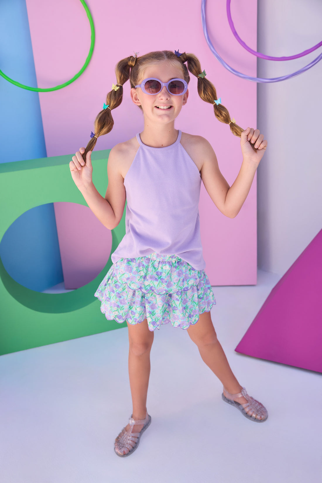 Model can be seen wearing a lavender halter tank top that features button closure along back and is made of a stretchy knit fabric. Top pairs back perfectly with tiered skort in the purple/aqua/green floral to complete the look. 