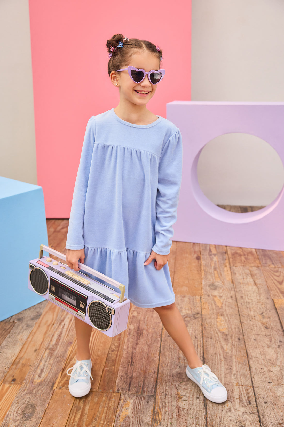 Model can be seen wearing long sleeve velour dress in periwinkle blue. Dress features button closure at back, and pleating detail across bust and bottom tier of dress for an elevated look. 