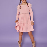 Model can be seen wearing soft knit ribbed pink dress that has sparkle star tulle along two tiers and the same tulle at sleeves for an angel sleeve effect. 