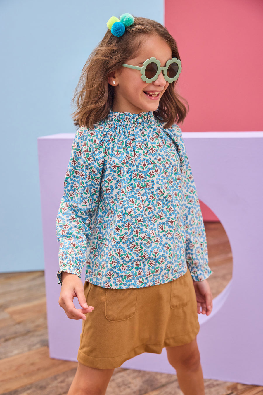 Model can be seen wearing brown/blue/green floral print woven shirt that features a high neck elastic collar which gives it the ruching affect. Top pairs back perfectly with brown faux suede skort to complete the look. 