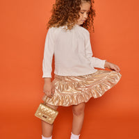 Model can be seen wearing knit pointelle white top with an elastic high neckline  and elastic cuffs paired back with a gold tiered lurex skirt with built in shorts. 