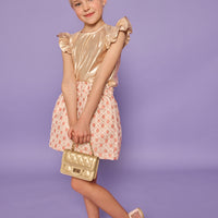 Model can be seen wearing gold metallic lurex top that features angel sleeve detail and button closure at back. Paired back with jacquard skirt with pink and gold metallic details.
