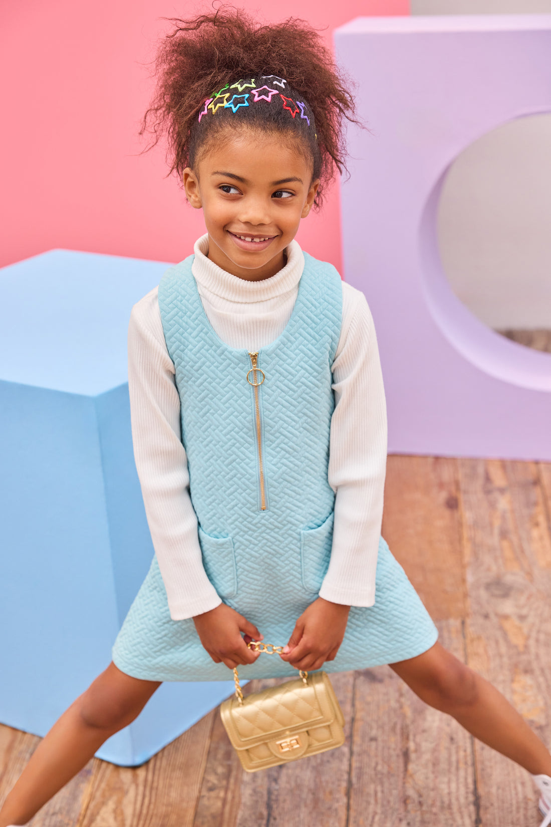 Model can be seen wearing a knit quilted jumper in an aqua color that features a gold quarter zip zipper and  two functional pockets in the front for an elevated look. Pair a ribbed turtleneck underneath to complete the look.