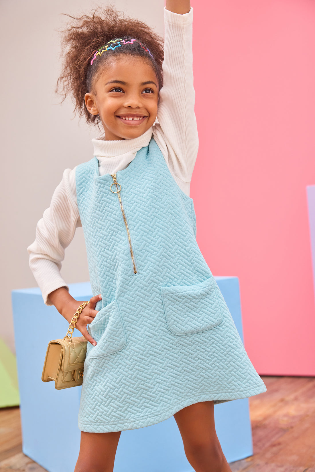 Model can be seen wearing a knit quilted jumper in an aqua color that features a gold quarter zip zipper and  two functional pockets in the front for an elevated look. Pair a ribbed turtleneck underneath to complete the look.