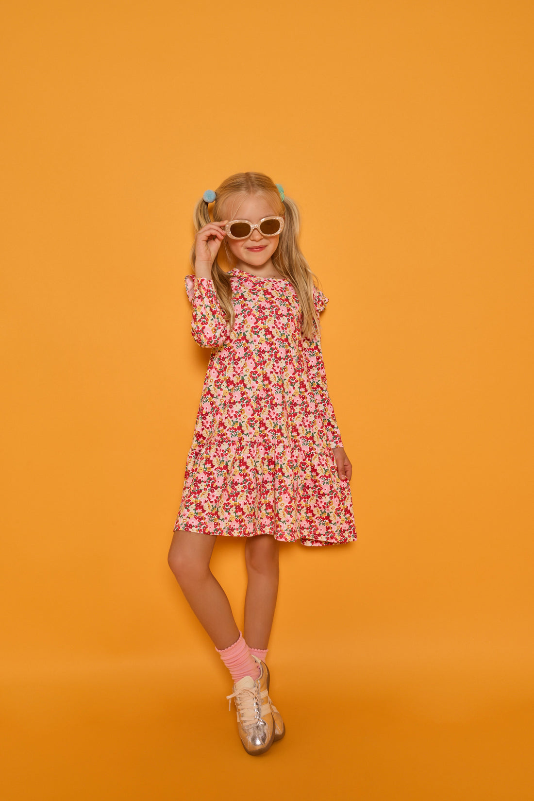 Model can be seen wearing a long sleeve knit floral dress in a fun pink/red/yellow print. Dress features ruffles at the top of the sleeves for an elevated look.