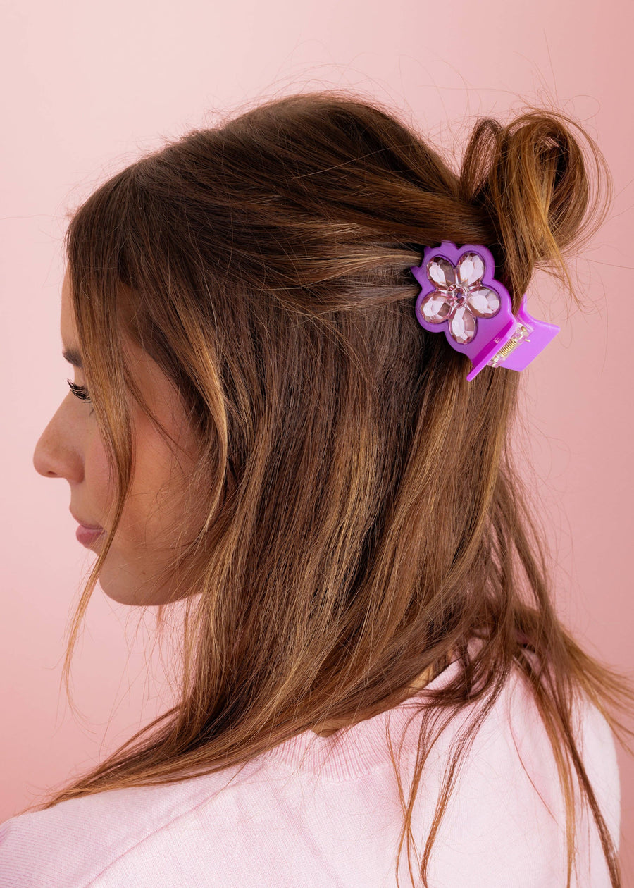 Woman with brown hair with a purple hair clip against a pink background