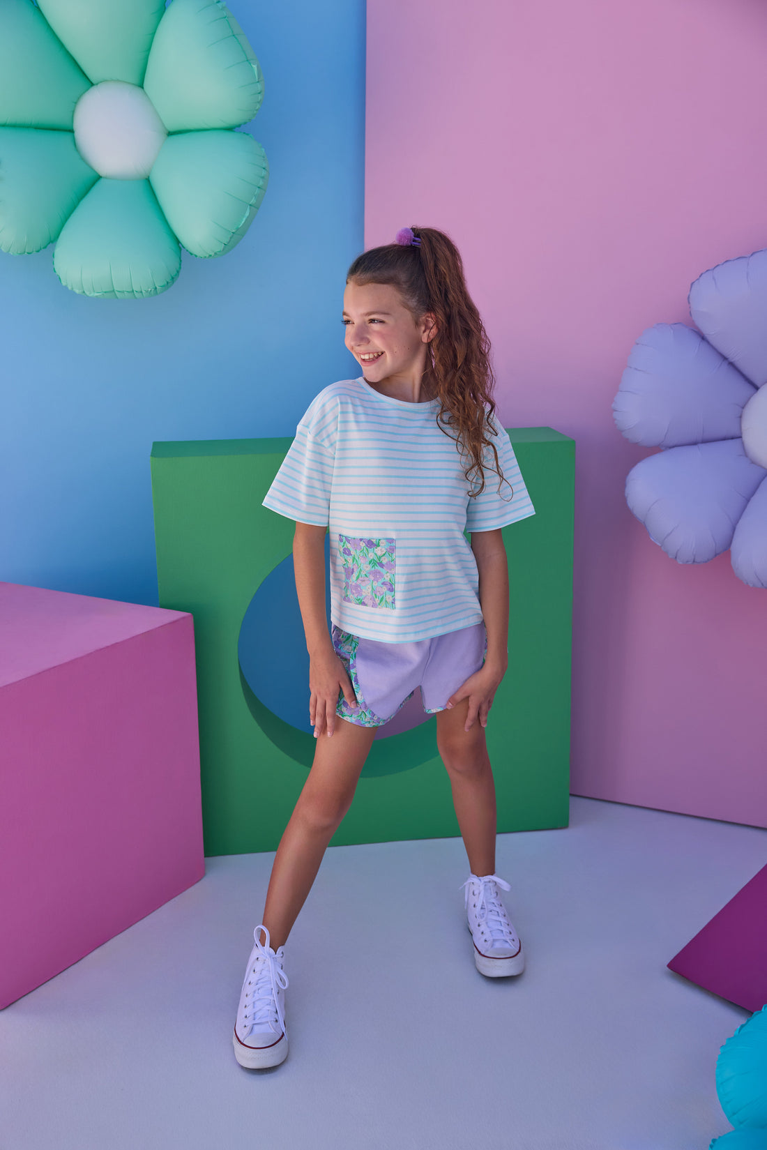 Model can be seen wearing pink and white stripe knit boxy tee that features a floral patch pocket that matches back perfectly with the aqua/purple floral trim on the track shorts to complete the look. 