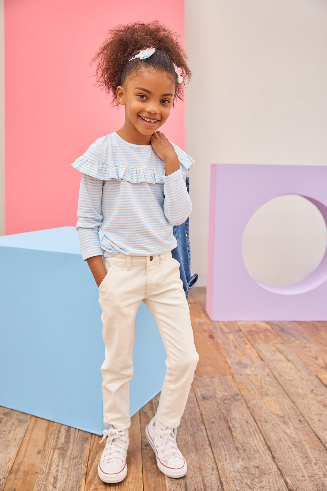 Tween girl seen wearing a pale blue and white stripe ruffle long sleeve t-shirt paired back with ivory denim jeans for an elevated but comfy look. 