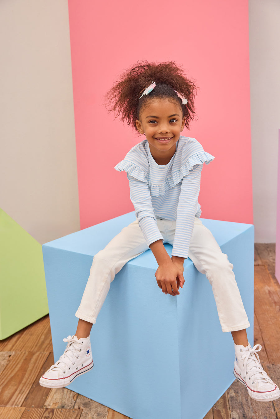 Tween girl seen wearing a pale blue and white stripe ruffle long sleeve t-shirt paired back with ivory denim jeans for an elevated but comfy look. 
