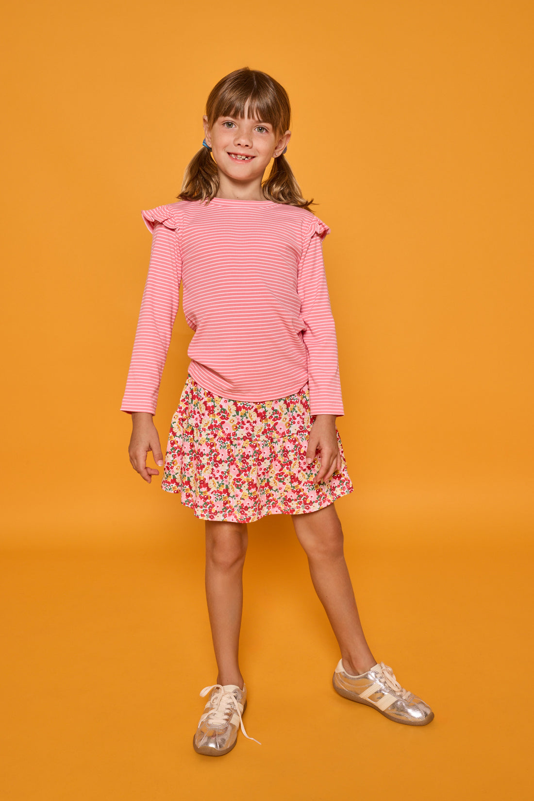 Model can be seen wearing a long sleeve pink and white stripe knit t-shirt that features ruffles at the sleeves. Paired back with our skort in a red/pink/yellow floral print, that has built in shorts, to complete the look.