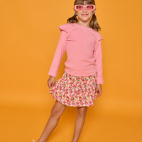 Model can be seen wearing a long sleeve pink and white stripe knit t-shirt that features ruffles at the sleeves. Paired back with our skort in a red/pink/yellow floral print, that has built in shorts, to complete the look.