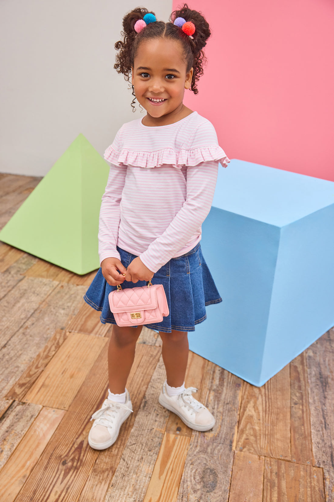 Model can be seen wearing a pleated denim mini skirt that features faux buttons to elevate the look, elastic waistband, and built in shorts. Skort pairs back perfectly with a knit pink and white striped long sleeve shirt that features a ruffle detail across bust to complete the look. 