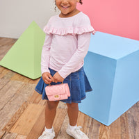 Model can be seen wearing a pleated denim mini skirt that features faux buttons to elevate the look, elastic waistband, and built in shorts. Skort pairs back perfectly with a knit pink and white striped long sleeve shirt that features a ruffle detail across bust to complete the look. 