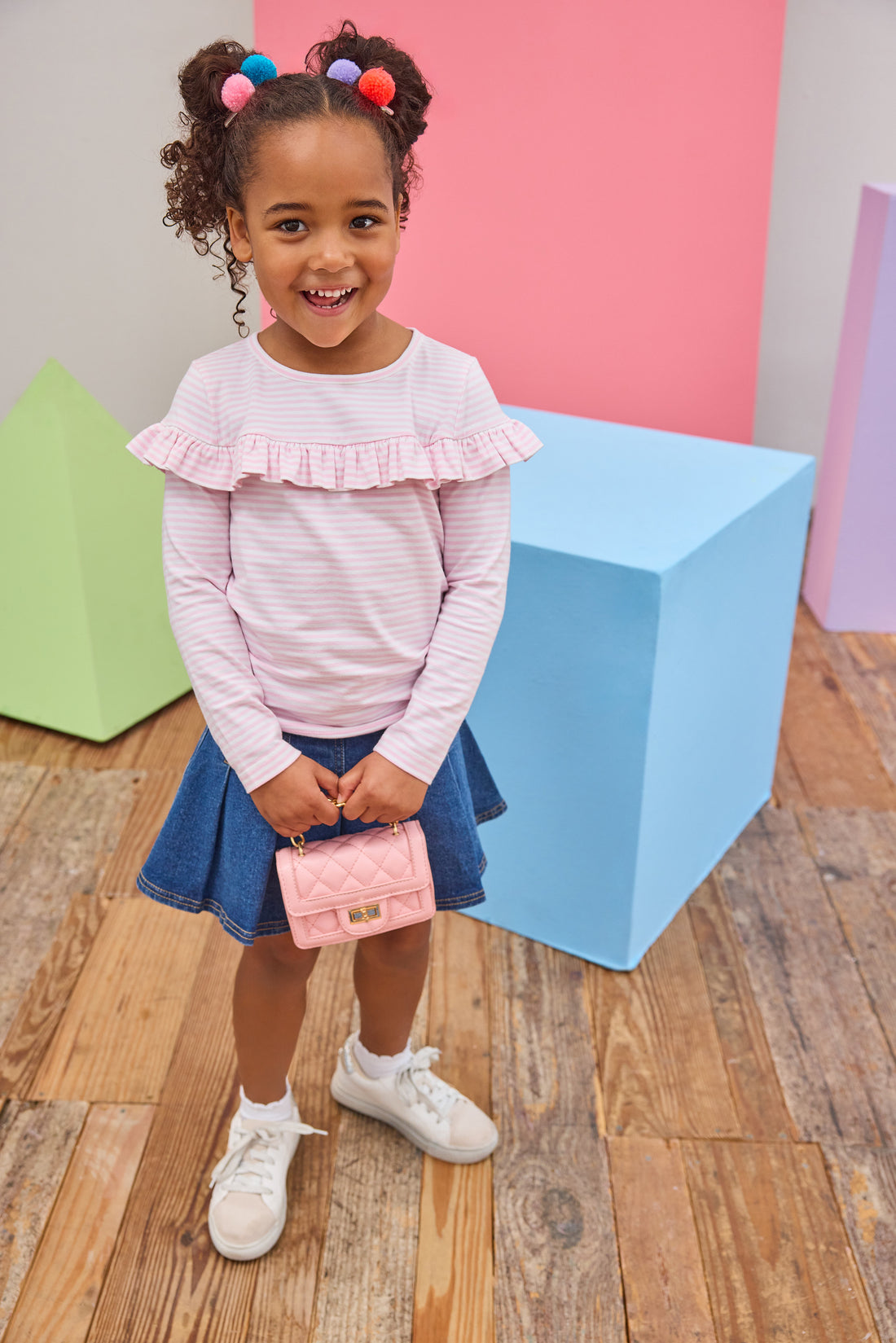 Tween girl seen wearing a pale pink and white stripe ruffle long sleeve t-shirt paired back with a pleated denim skort to elevate the look. 