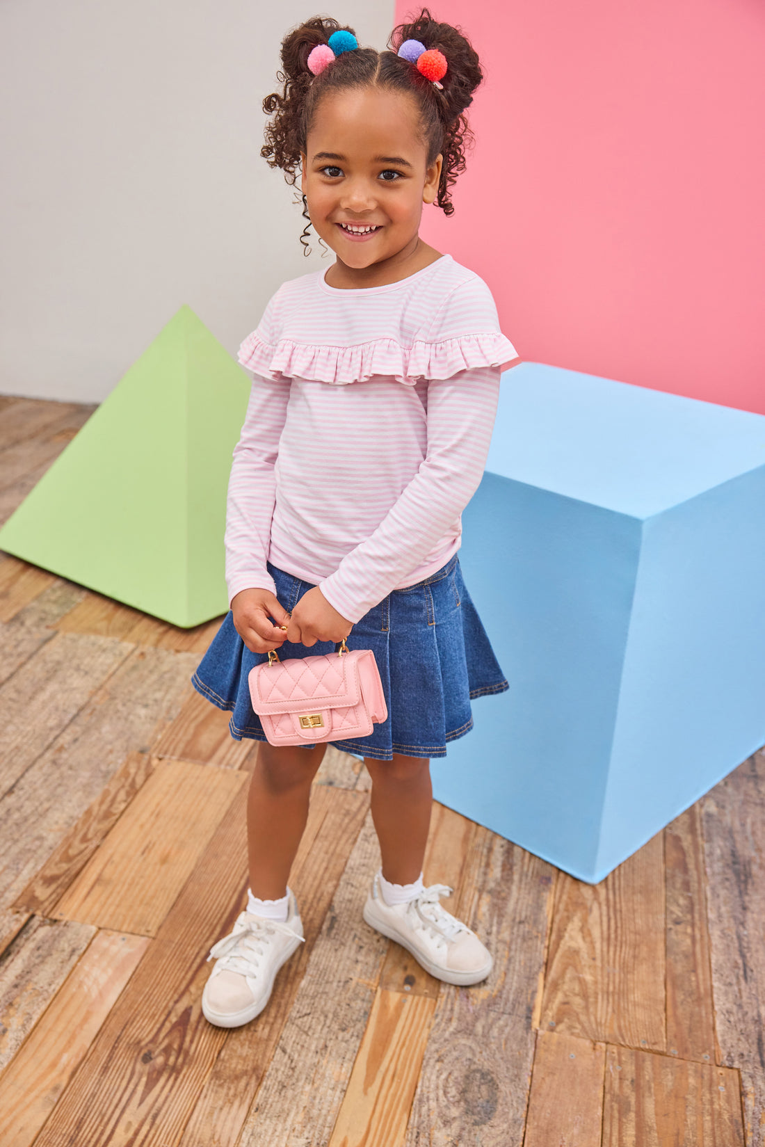 Tween girl seen wearing a pale pink and white stripe ruffle long sleeve t-shirt paired back with a pleated denim skort to elevate the look. 