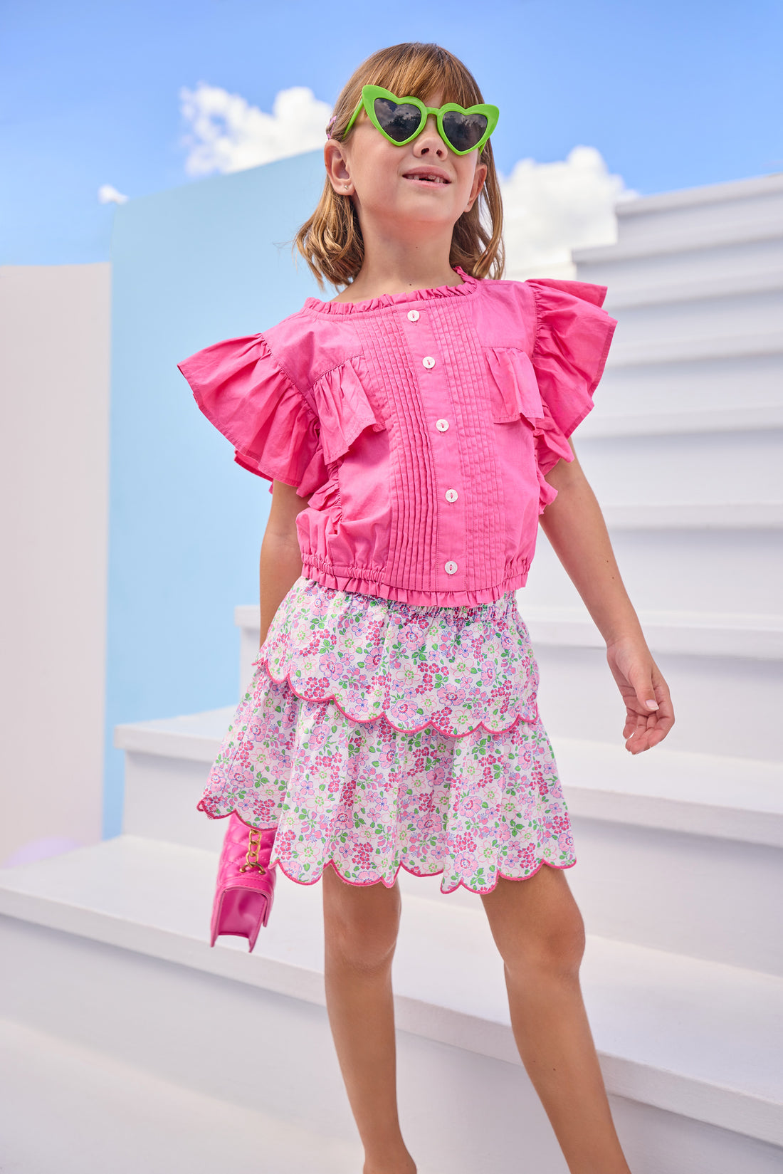 Model can be seen wearing hot pink woven top that features button closures down the front and big angel sleeve detail to elevate the look. Top pairs back perfectly with pink floral print on skort to complete the look.