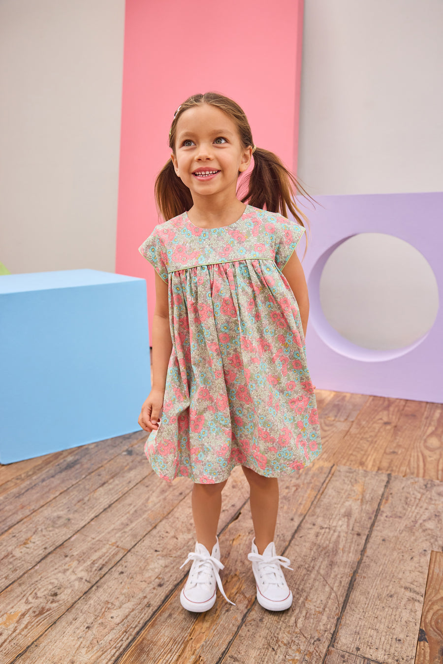 Model can be seen wearing a woven short sleeve dress in a gorgeous salmon pink/teal/green floral print that features button closures along back and green  trim detail across bust and along sleeves for an elevated look. 