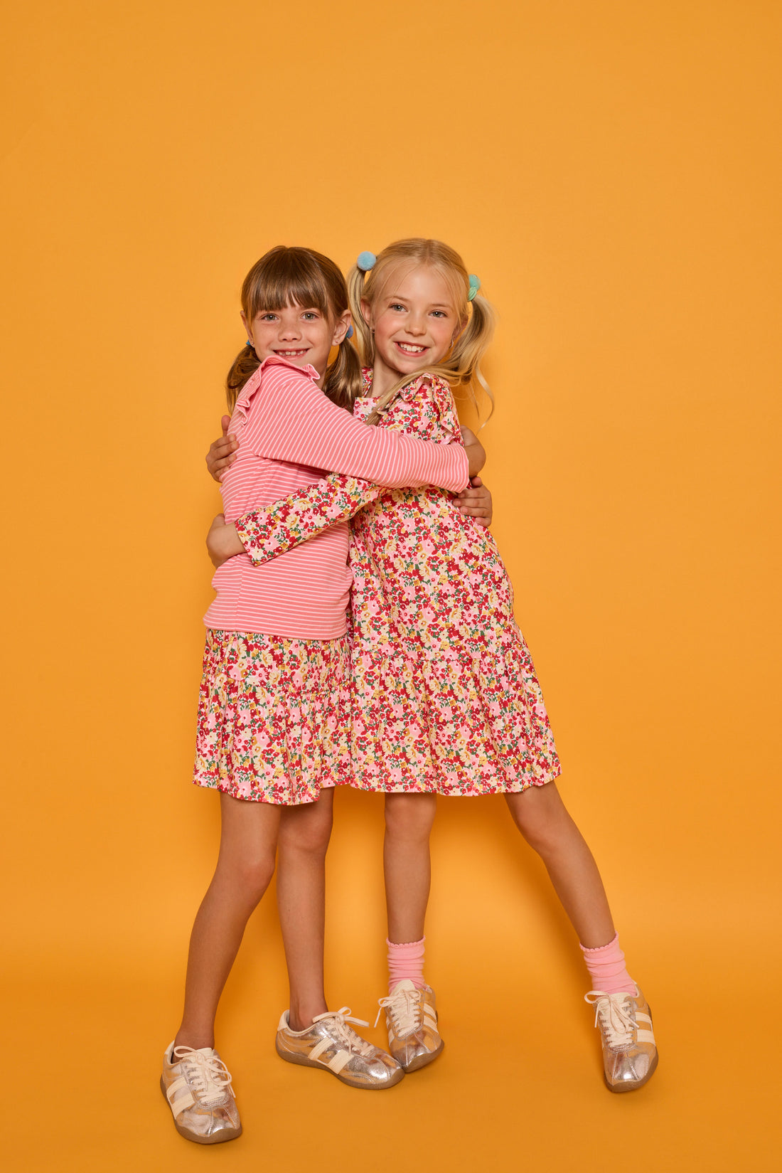 Model on right can be seen wearing long sleeve knit dress in red/yellow/floral print while the model on the left can be seen wearing a long sleeve pink and white stripe knit t-shirt that features ruffles at the sleeves. Paired back with our skort in a red/pink/yellow floral print, that has built in shorts, to complete the look.