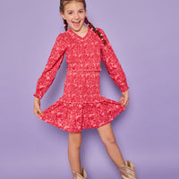 Model can be seen wearing a red/pink floral woven ruched dress. Dress features elastic ruching throughout, a v-neck neckline, and elastic cuffs at sleeves. 