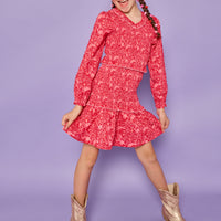 Model can be seen wearing a red/pink floral woven ruched dress. Dress features elastic ruching throughout, a v-neck neckline, and elastic cuffs at sleeves. 