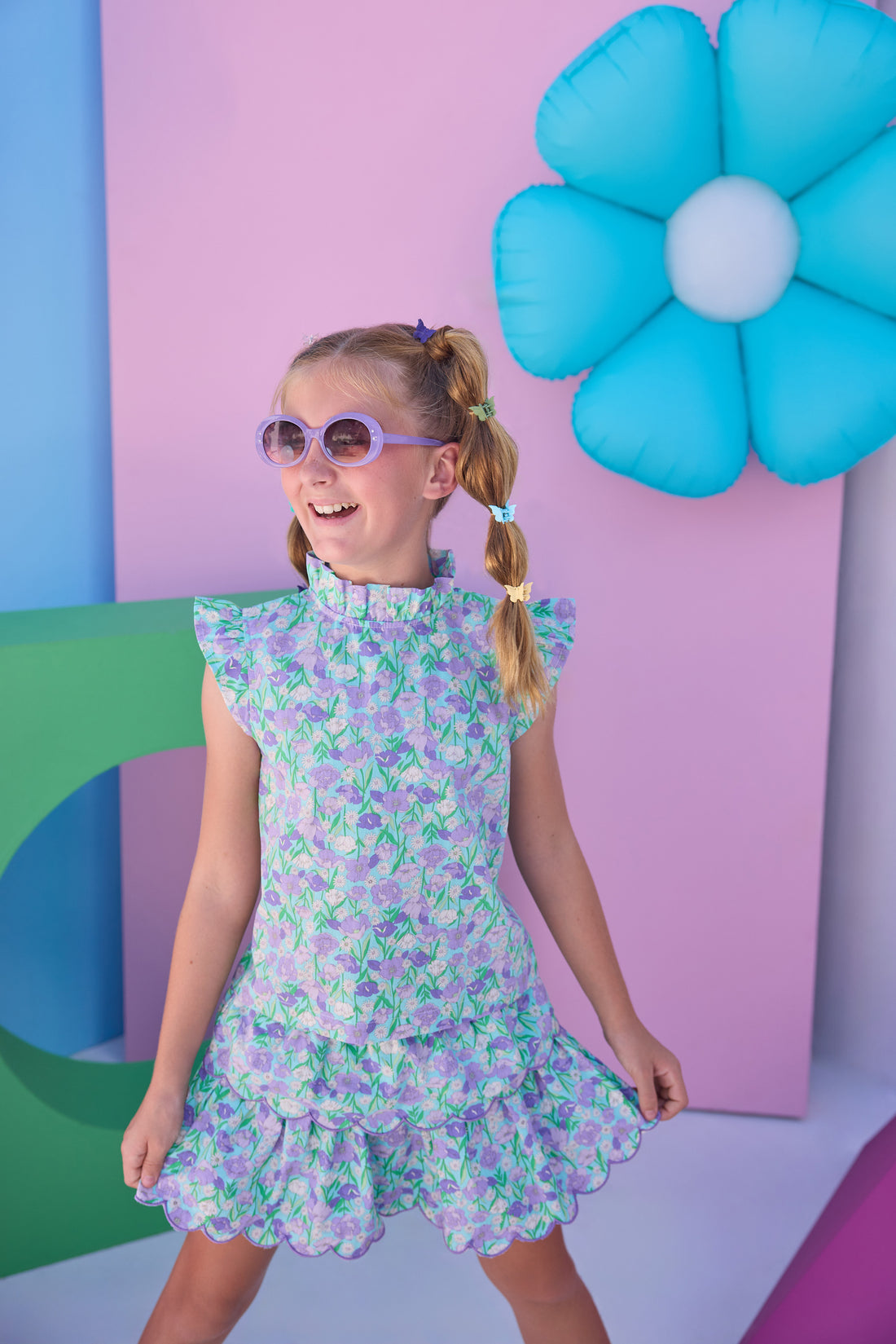 Model can be seen wearing a woven aqua/purple floral top that features angel sleeve details, high ruffle neckline, and button closure on back for a comfy but secure fit. Matches back perfectly with the tiered skort in the same floral print to complete the look.