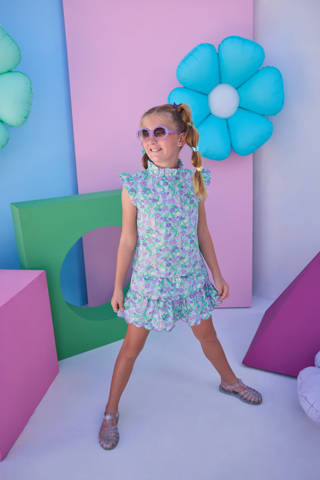 Model can be seen wearing a woven aqua/purple floral top that features angel sleeve details, high ruffle neckline, and button closure on back for a comfy but secure fit. Matches back perfectly with the tiered skort in the same floral print to complete the look.