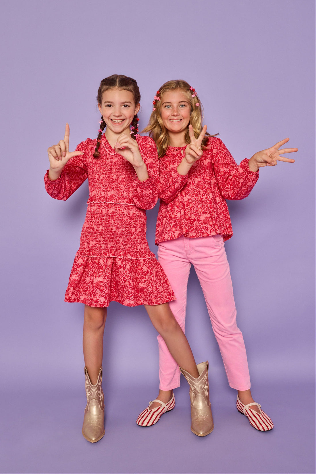 Models can be seen wearing a red and pink floral print in either a woven ruched dress on the left or a woven long sleeve top on the right. The top features tie tassels in the front of the v-neckline for an elevated look, which pairs back perfectly with our corduroy pants in the matching pink color. 