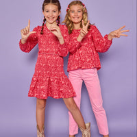 Models can be seen wearing a red and pink floral print in either a woven ruched dress on the left or a woven long sleeve top on the right. The top features tie tassels in the front of the v-neckline for an elevated look, which pairs back perfectly with our corduroy pants in the matching pink color. 
