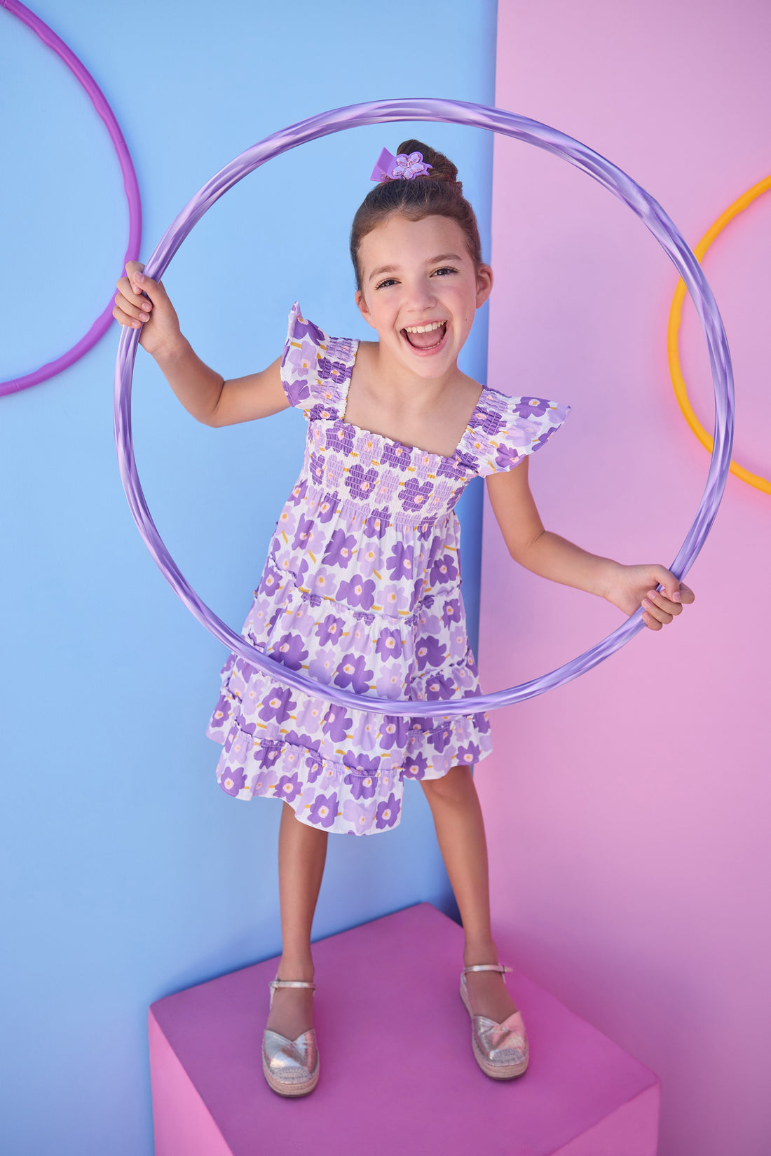 Model can be seen wearing a woven dress in a purple floral print. Dress features smocking detail across bust and slight angel sleeves to elevate the look. 