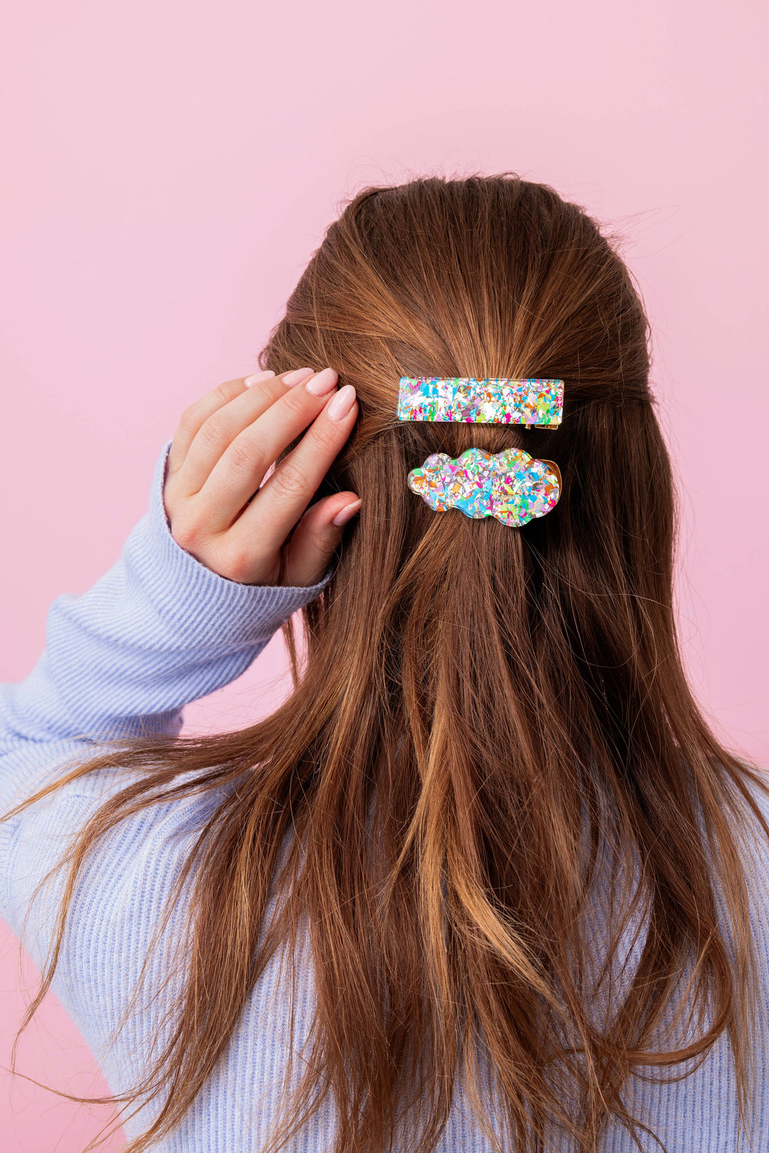 Person with long brown hair wearing colorful hair clips on a pink background